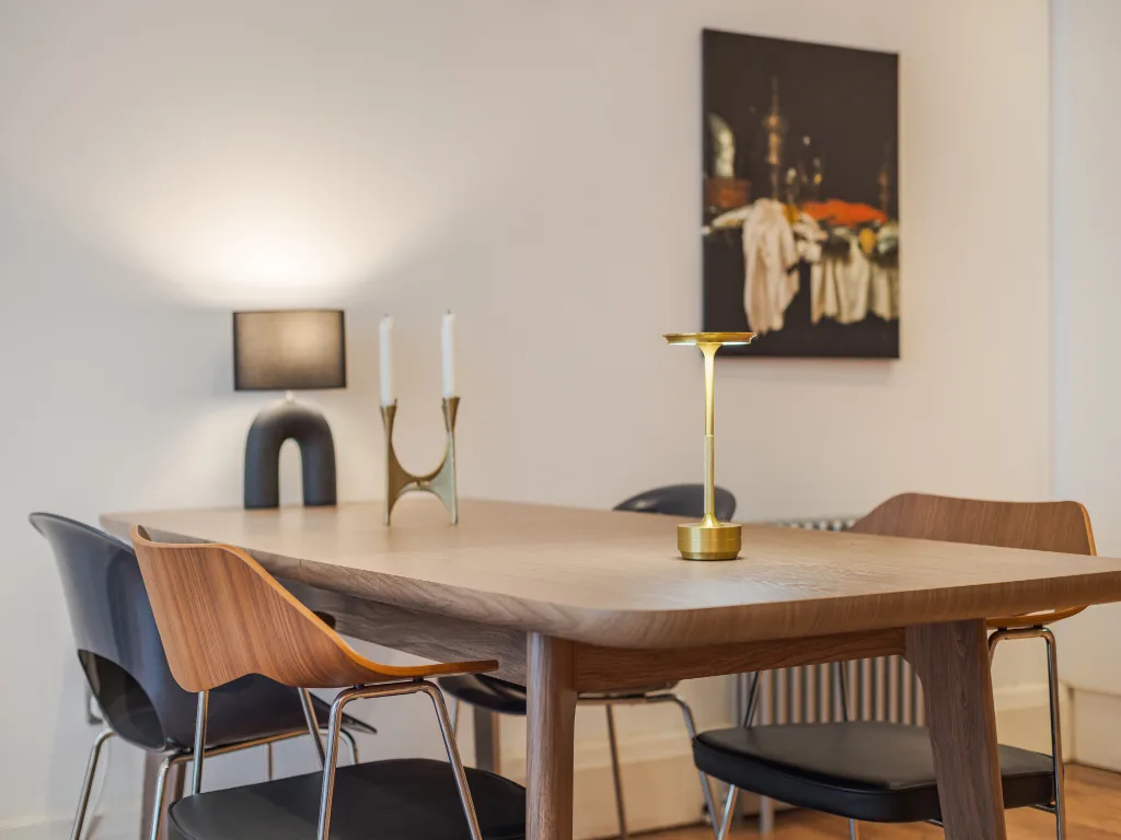 Un comedor con una mesa de madera, sillas y una lámpara de tono dorado.