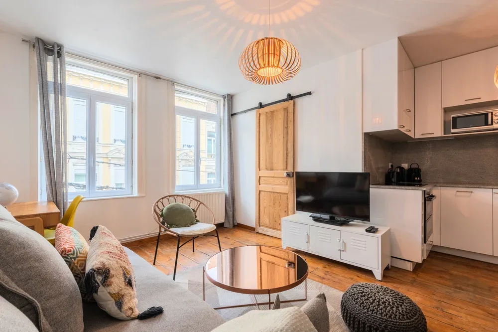 A bright living room with a television, seating, and tall windows.