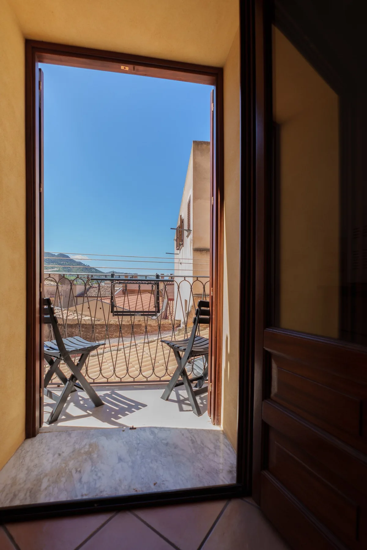Una puerta abierta da a un balcón con asientos y vistas al mar.