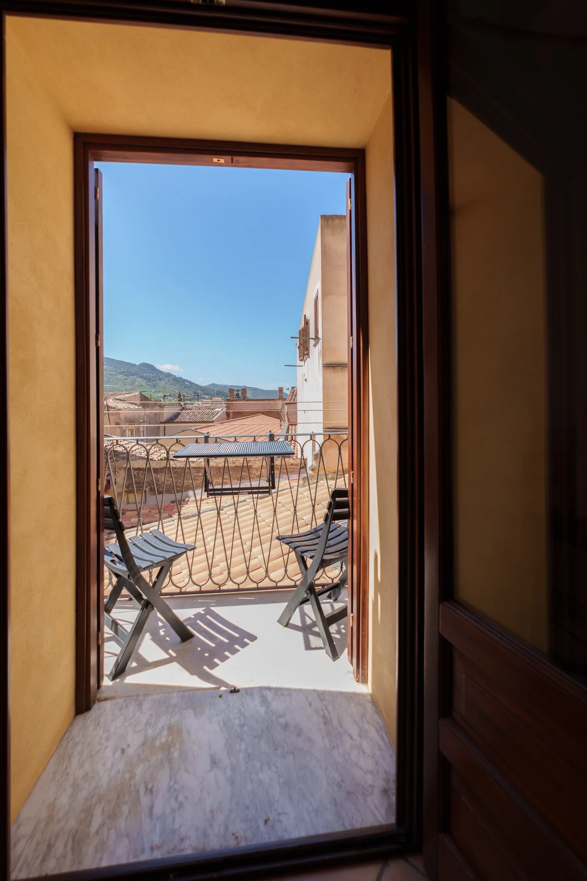 An open doorway leads to a sunlit terrace with outdoor seating and distant hills.