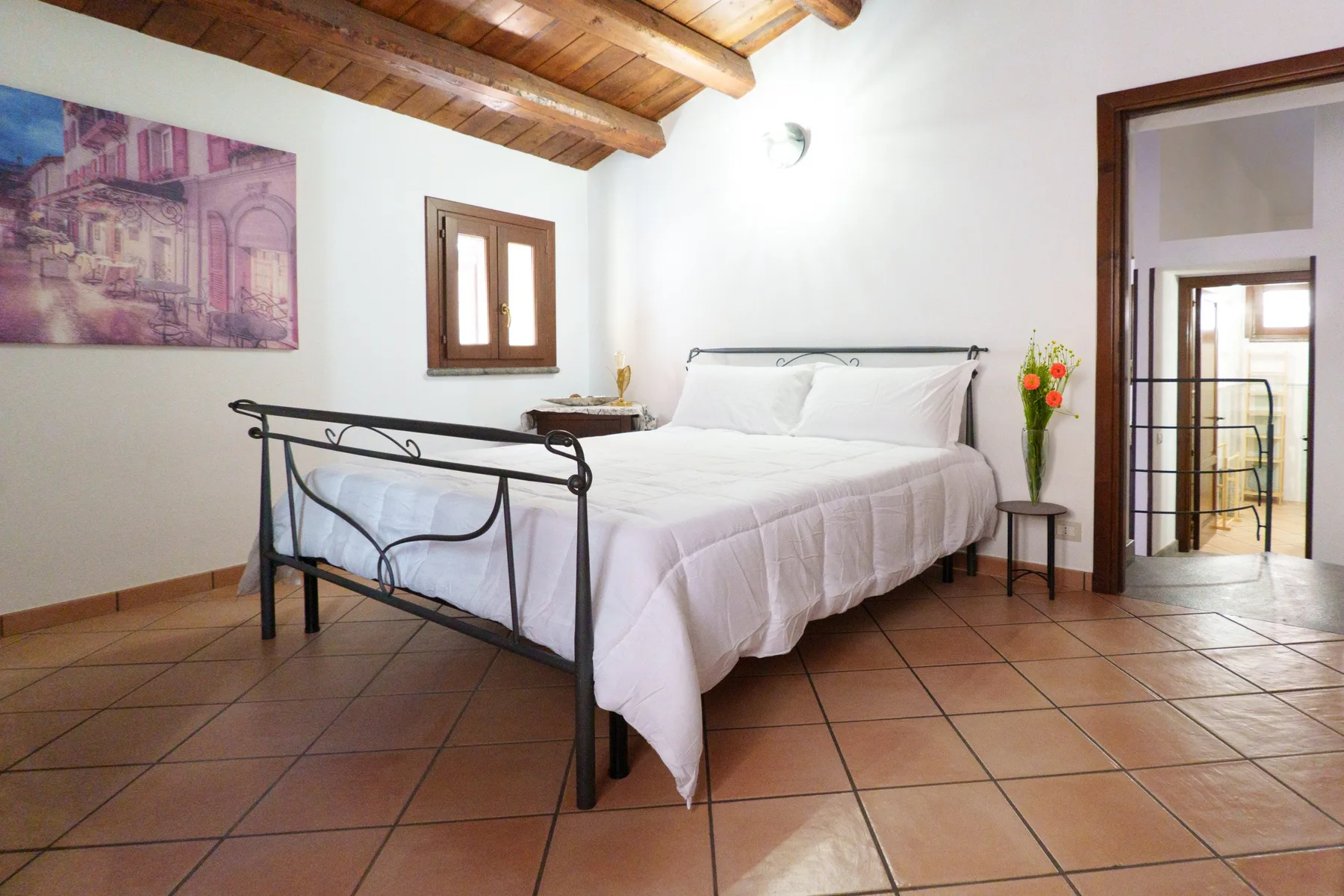 A bedroom with a bed, tiled floor, and exposed wooden ceiling beams.