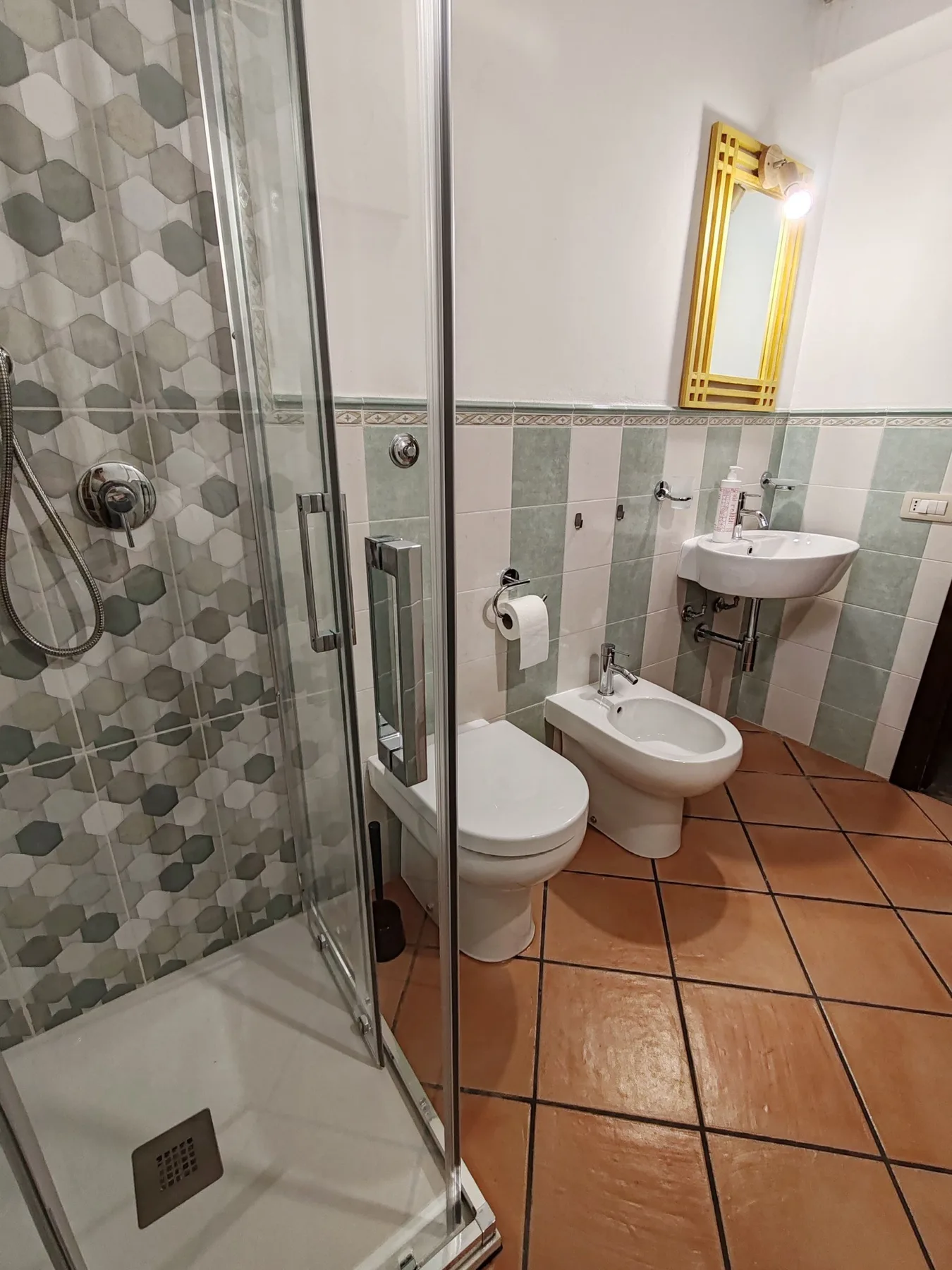 Un baño alicatado con ducha de vidrio, inodoro y lavabo mural.