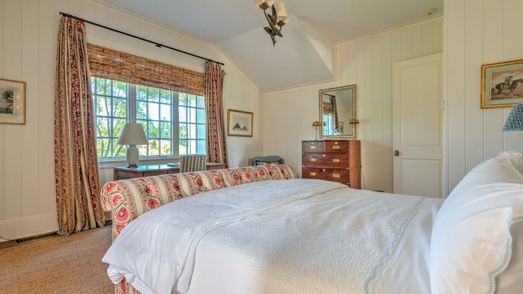 Un dormitorio con una cama grande, cortinas estampadas y una ventana con vistas a la vegetación.