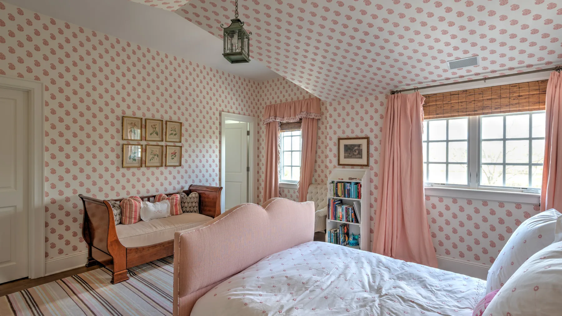 Un dormitorio con una cama, asientos y papel pintado estampado.