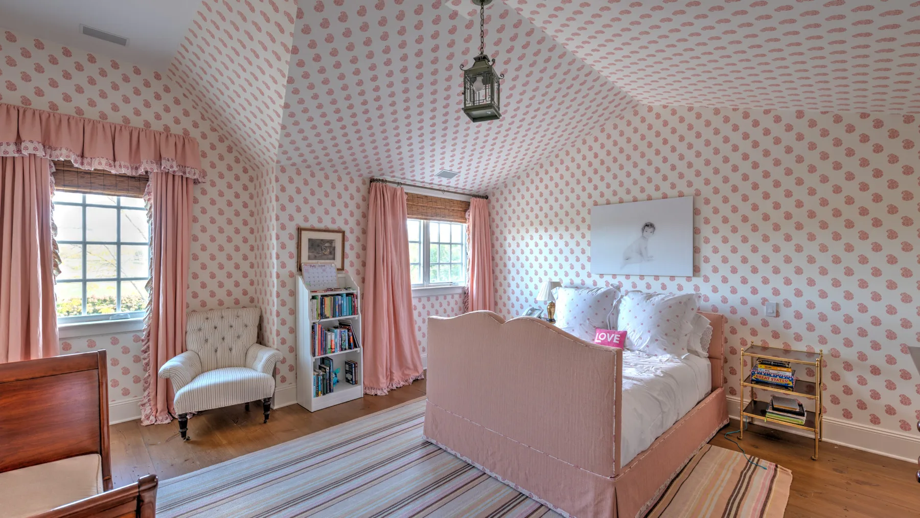 Un dormitorio rosa con una cama, una alfombra a rayas y paredes estampadas.