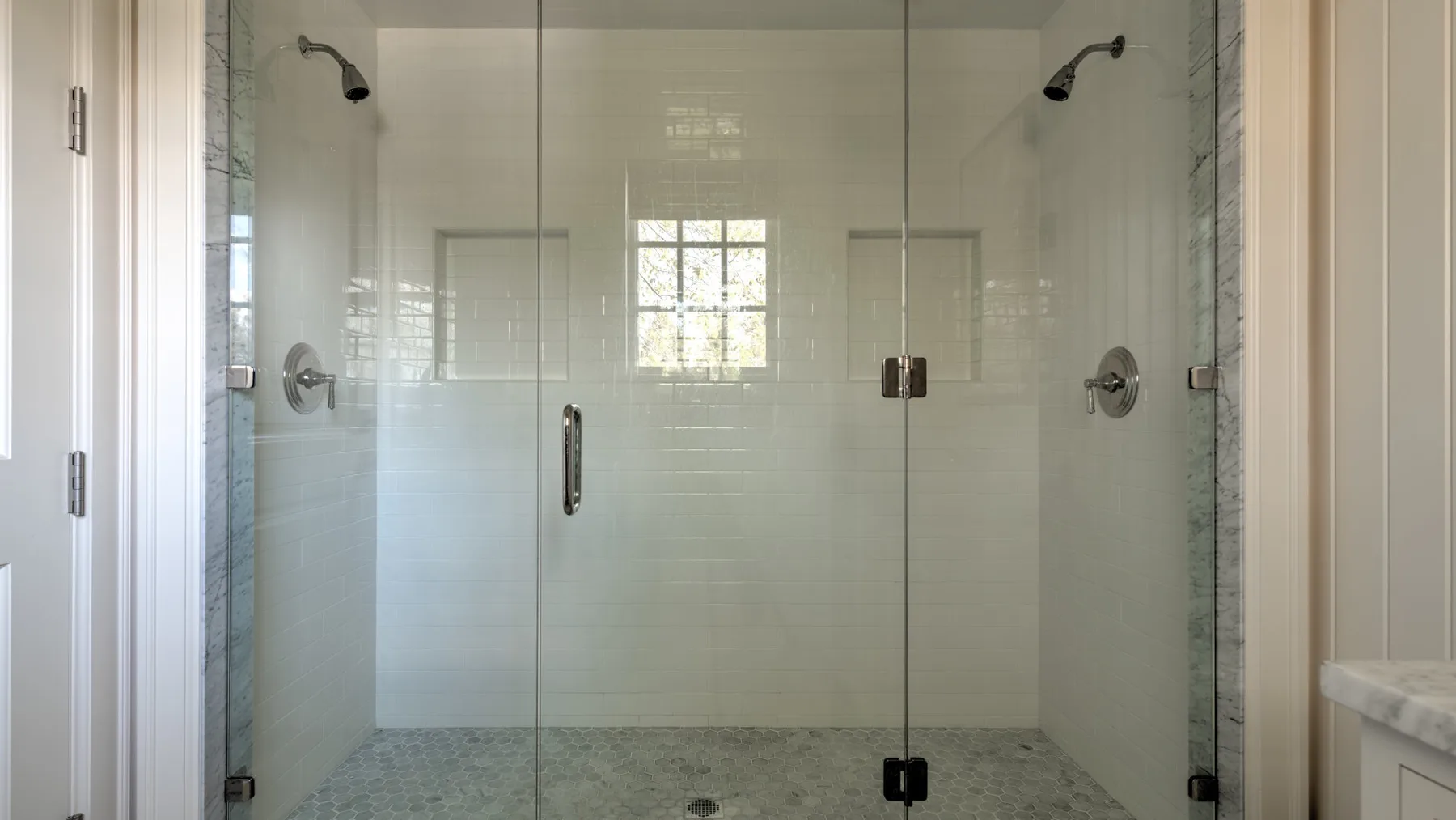 Una ducha con azulejos, puertas de vidrio y cabezales montados en la pared.