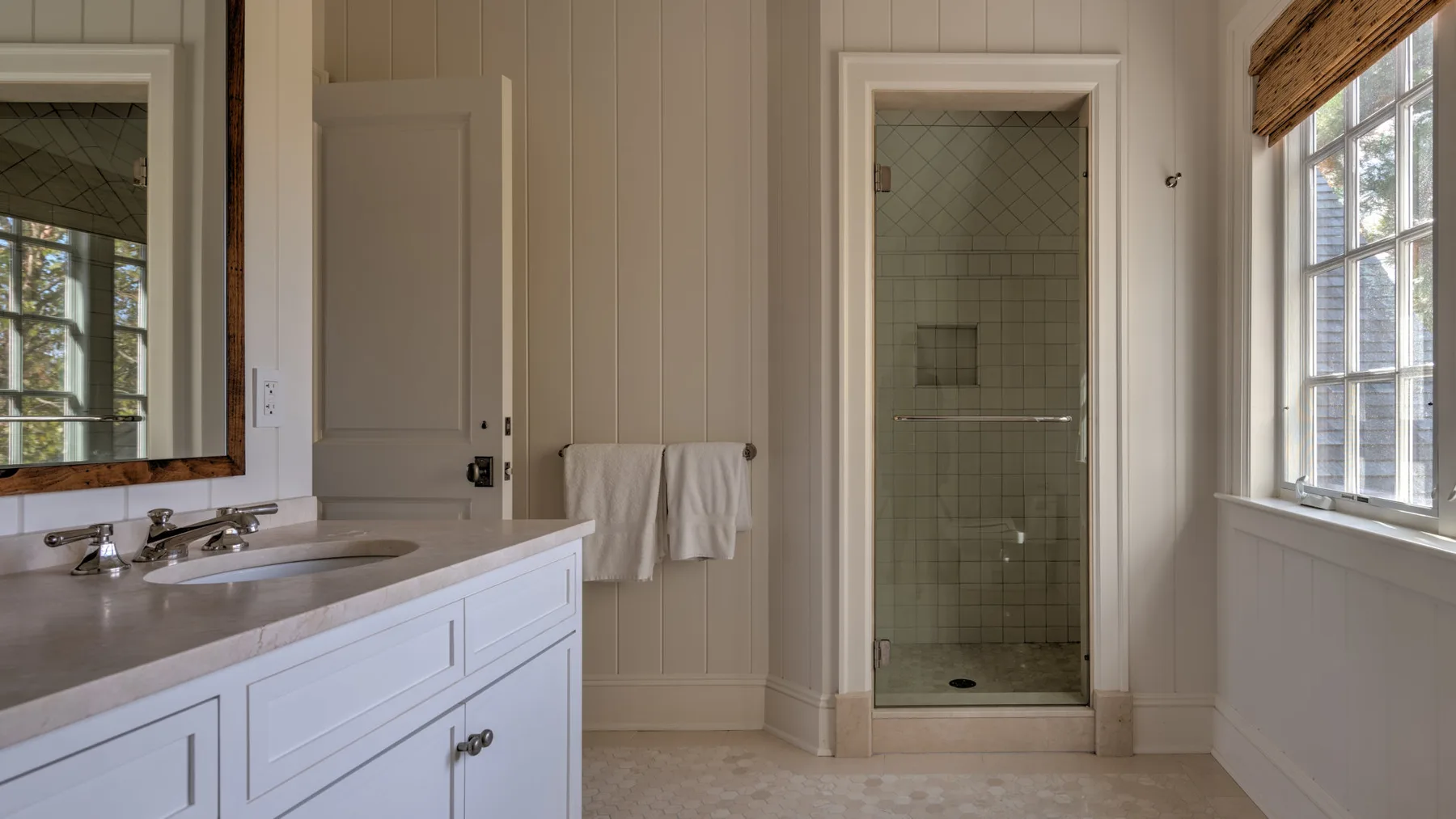 Un baño luminoso con un mueble de lavabo largo, espejo de pared y ducha de vidrio.