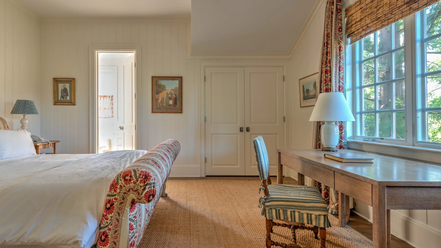 Un dormitorio con una cama, un escritorio y una silla junto a una ventana grande.