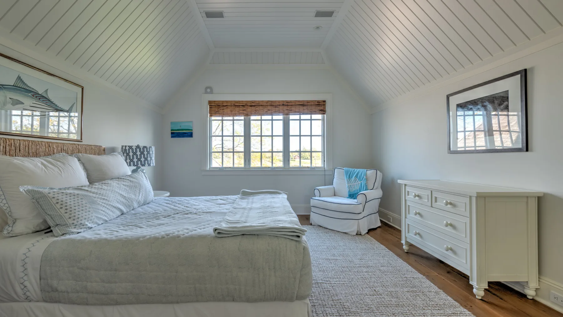 Un dormitorio luminoso con una cama, una zona de estar y una ventana grande.