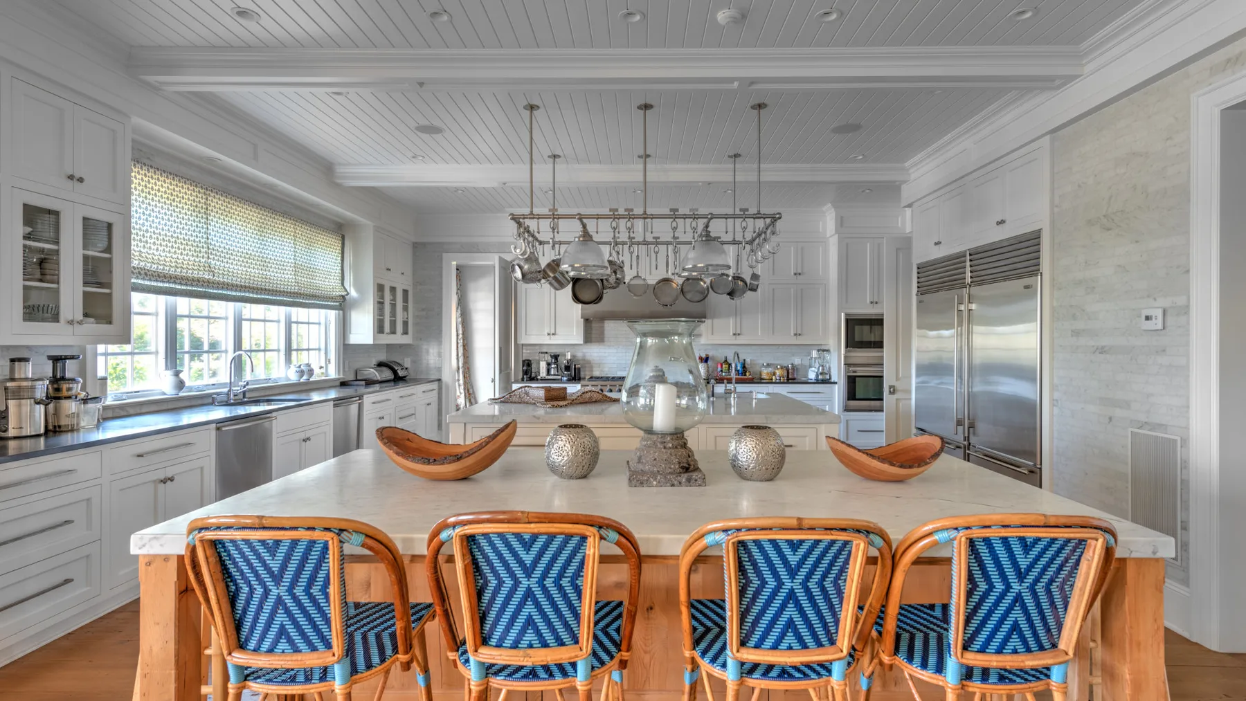 Una cocina luminosa con una isla grande, asientos estampados en azul y utensilios colgantes.