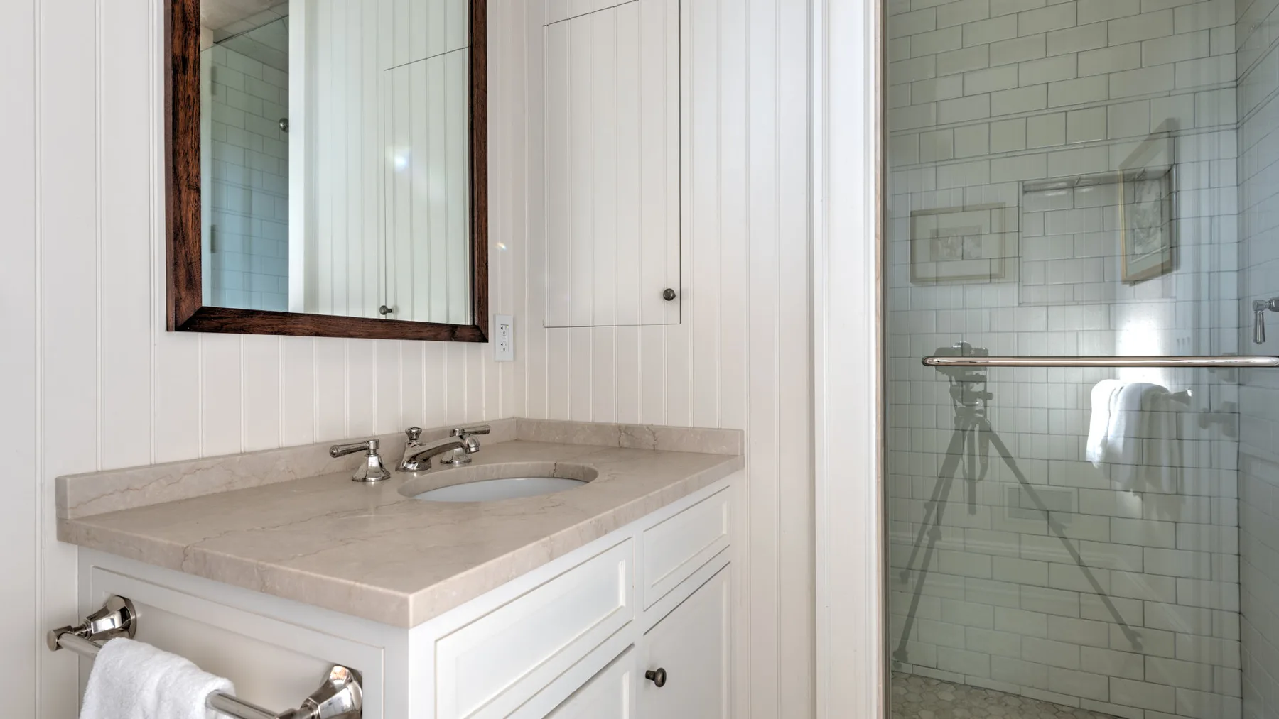 Un lavabo de baño luminoso con un espejo amplio junto a una ducha de vidrio.
