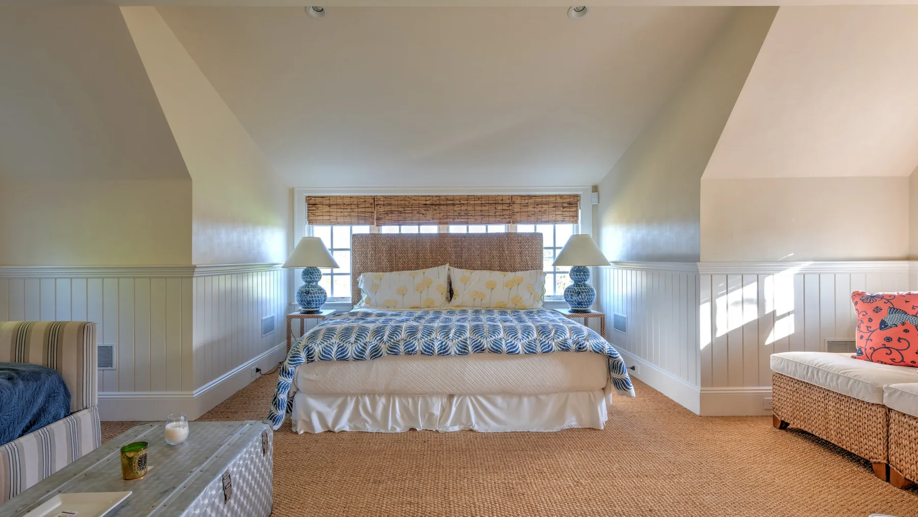 Un dormitorio con una cama bajo una ventana y asientos junto a las paredes.