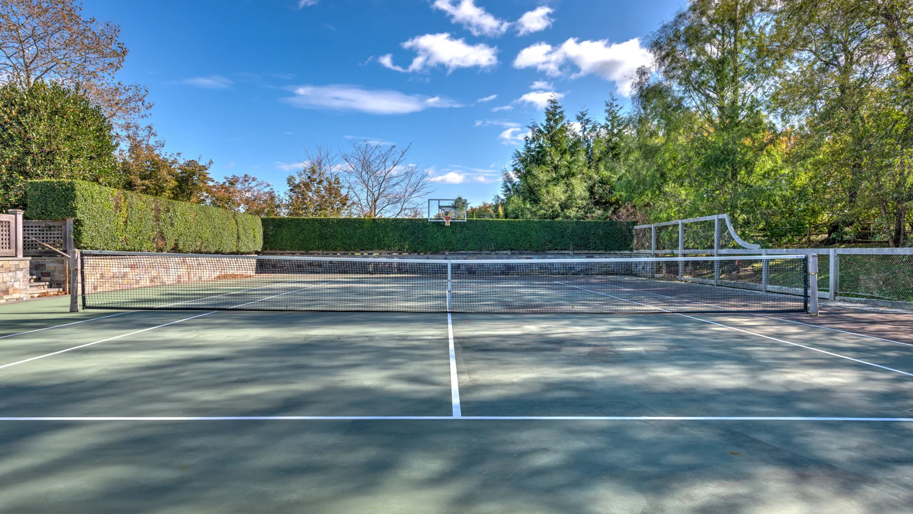 Una cancha de tenis al aire libre está rodeada de árboles y setos.