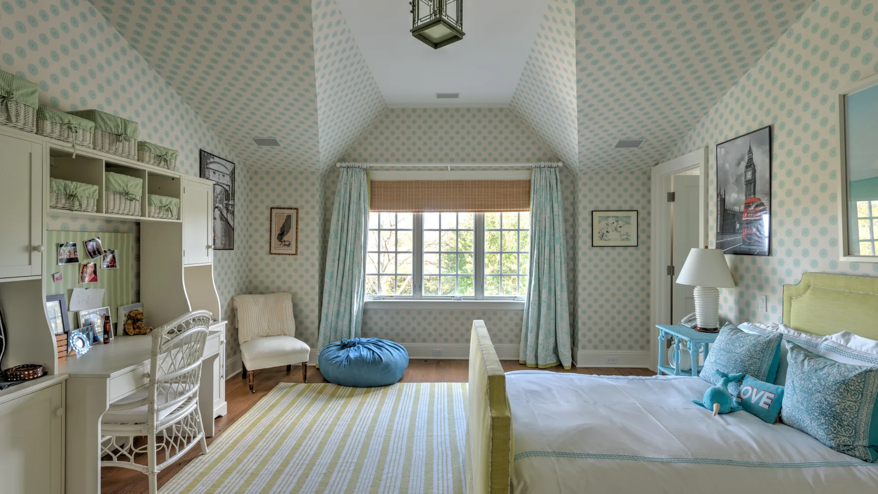 Un dormitorio luminoso con escritorio, una ventana grande y una cama.