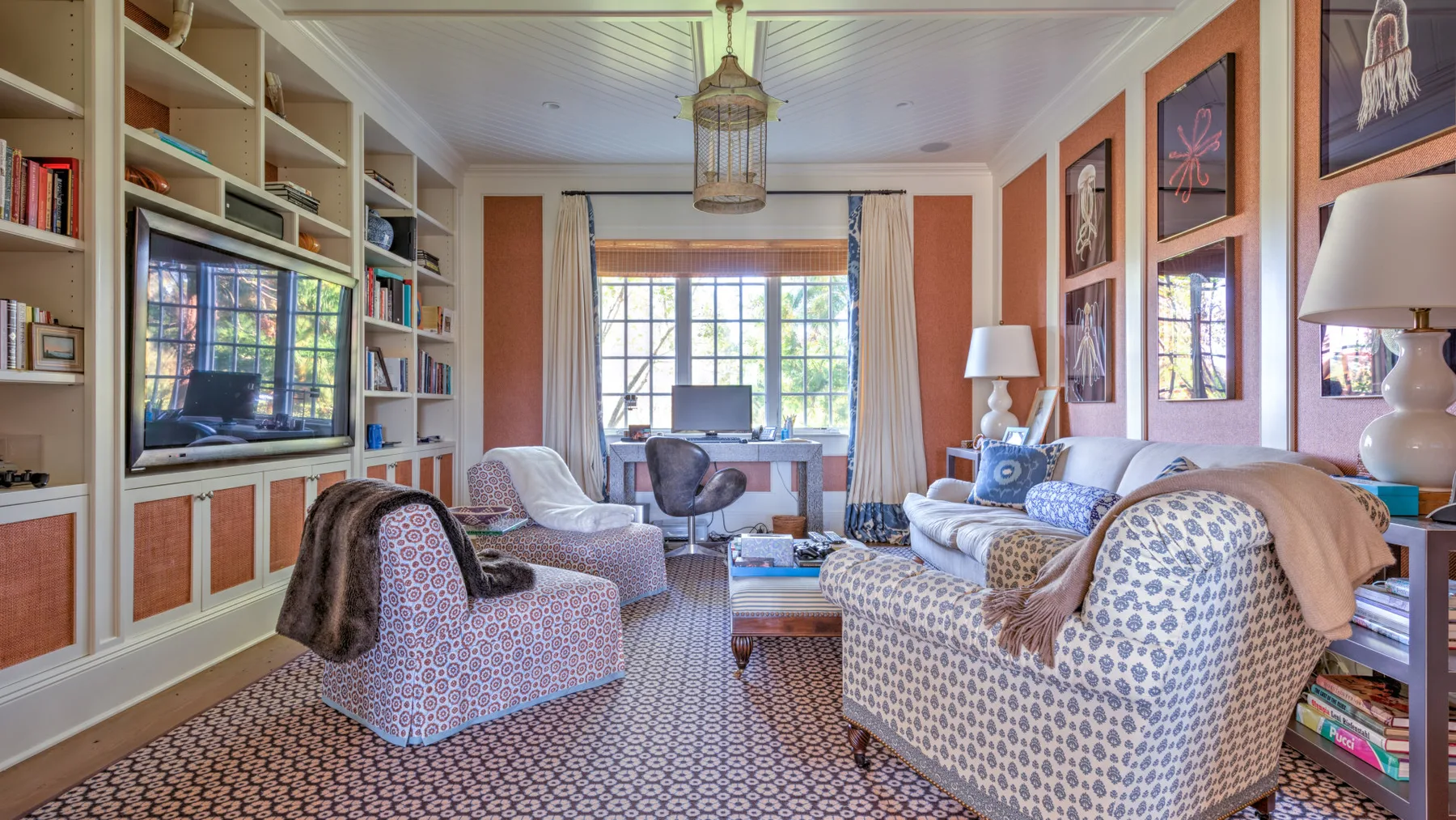 Una sala de estar con asientos estampados, estanterías empotradas y ventanas grandes.