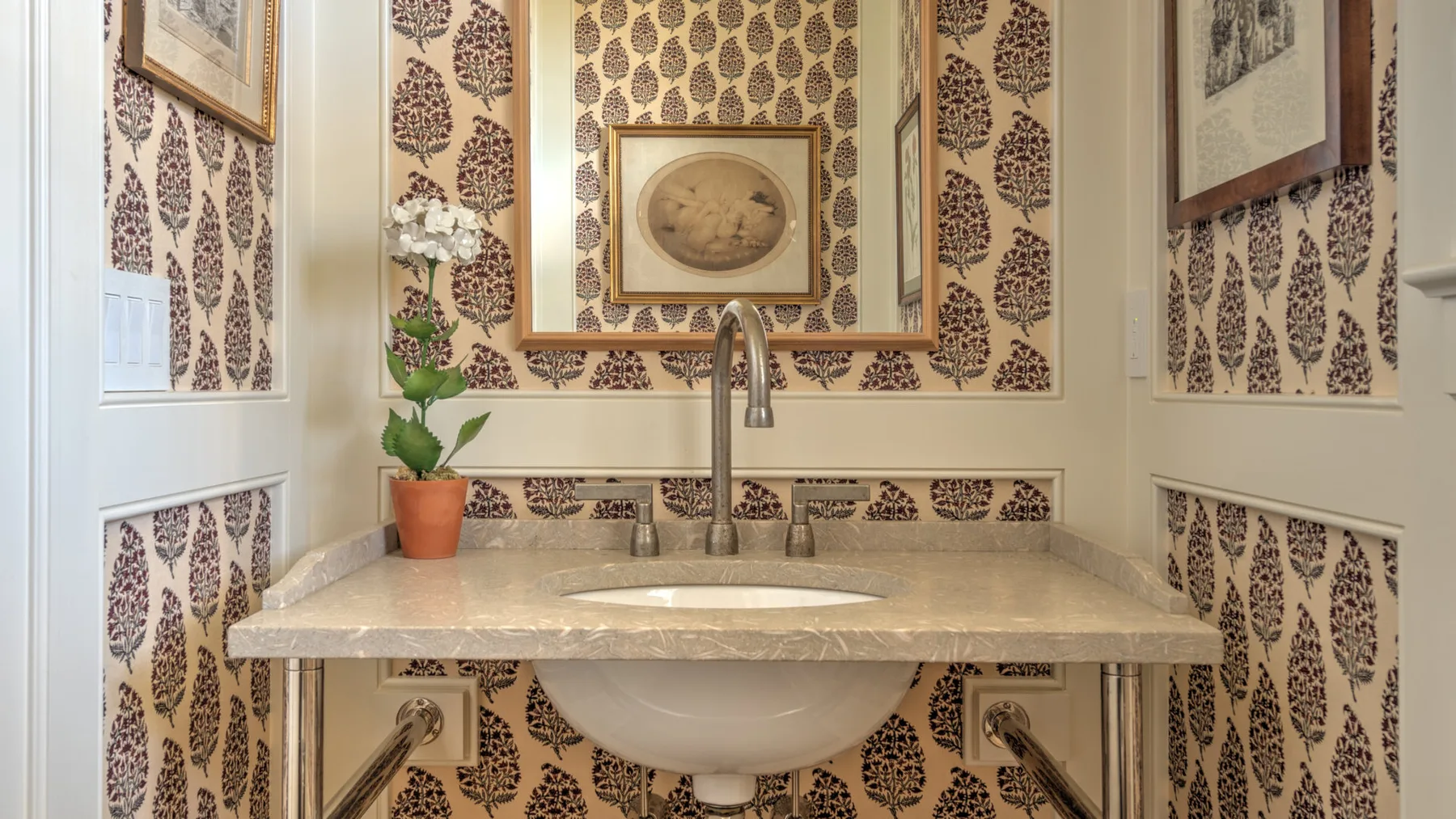 Un tocador de baño con encimera clara, lavabo y papel tapiz estampado.