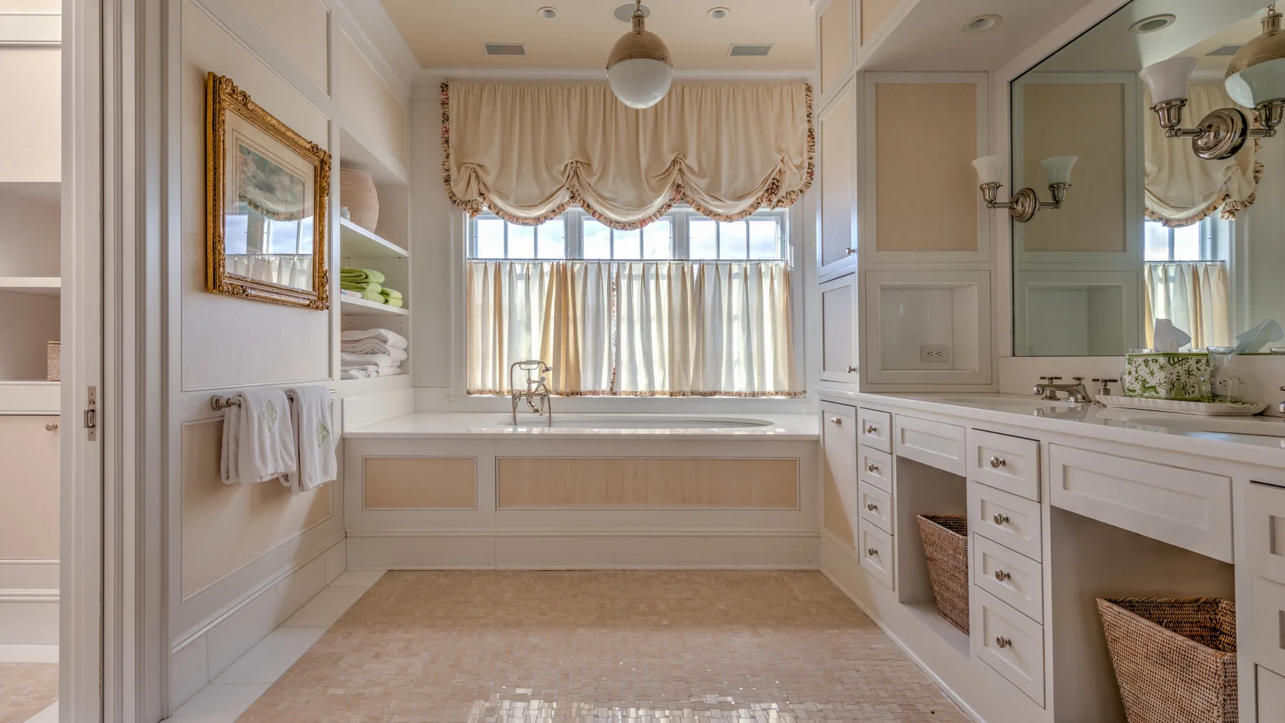 Un baño luminoso con una bañera bajo una ventana con cortinas y armarios blancos.