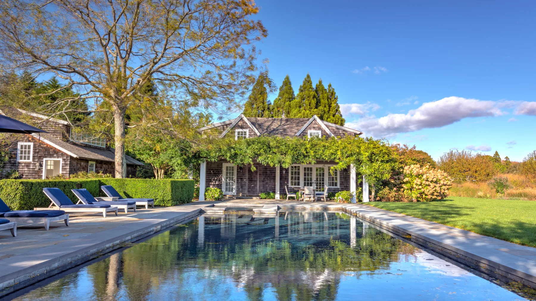 Una piscina al aire libre está junto a un patio ajardinado y una casa.