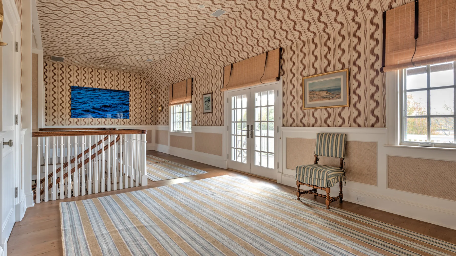 Una sala luminosa con paredes estampadas, puertas francesas y una alfombra a rayas.