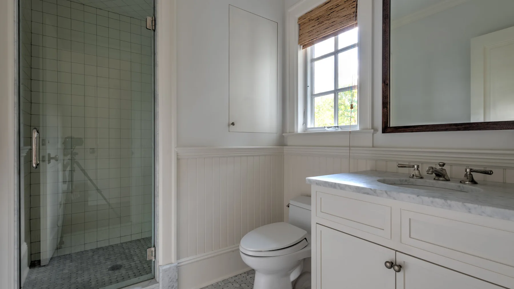 Un baño con ducha de vidrio, inodoro y lavabo bajo una ventana.
