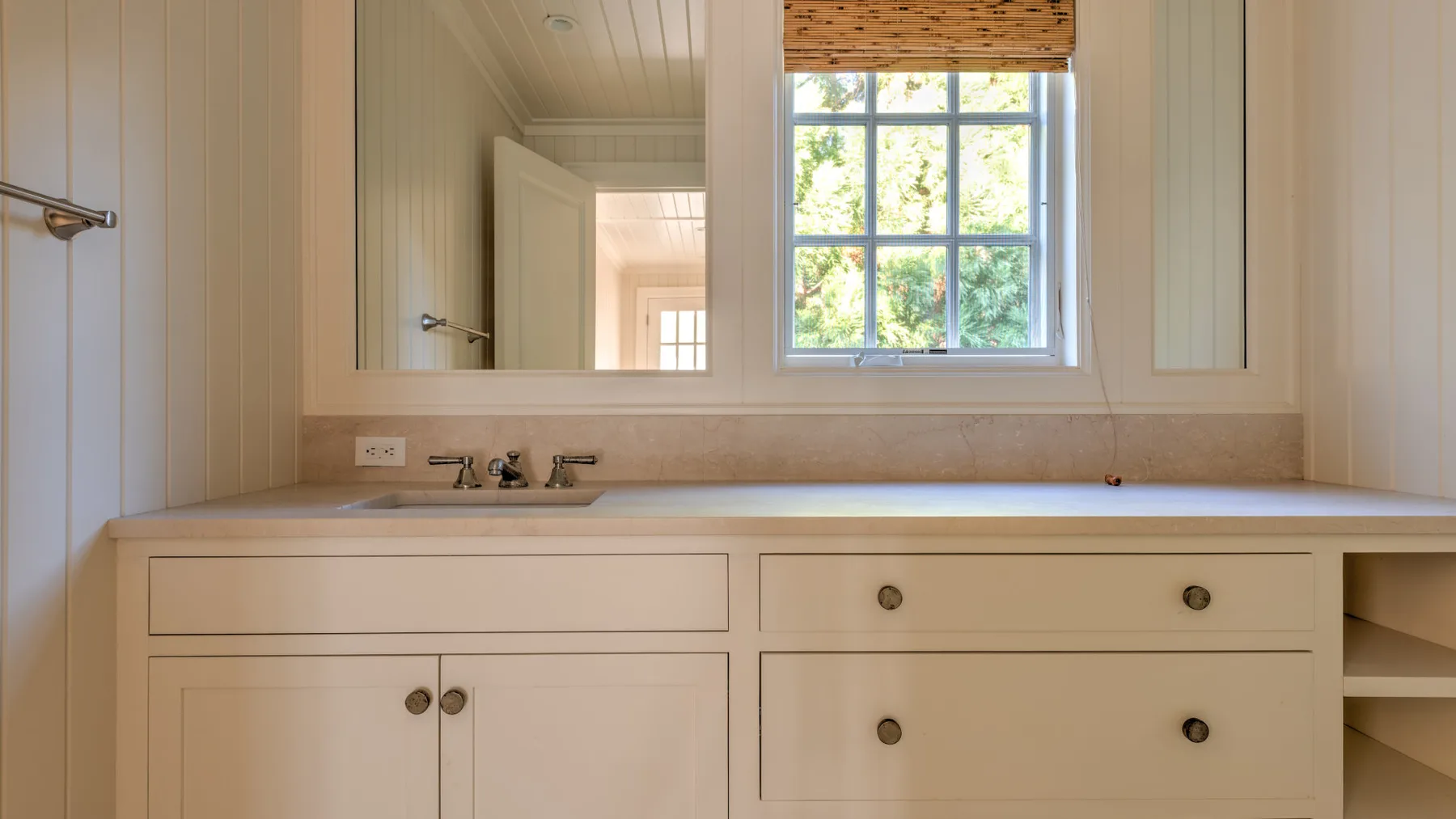 Un tocador de baño luminoso con un espejo amplio y una ventana.