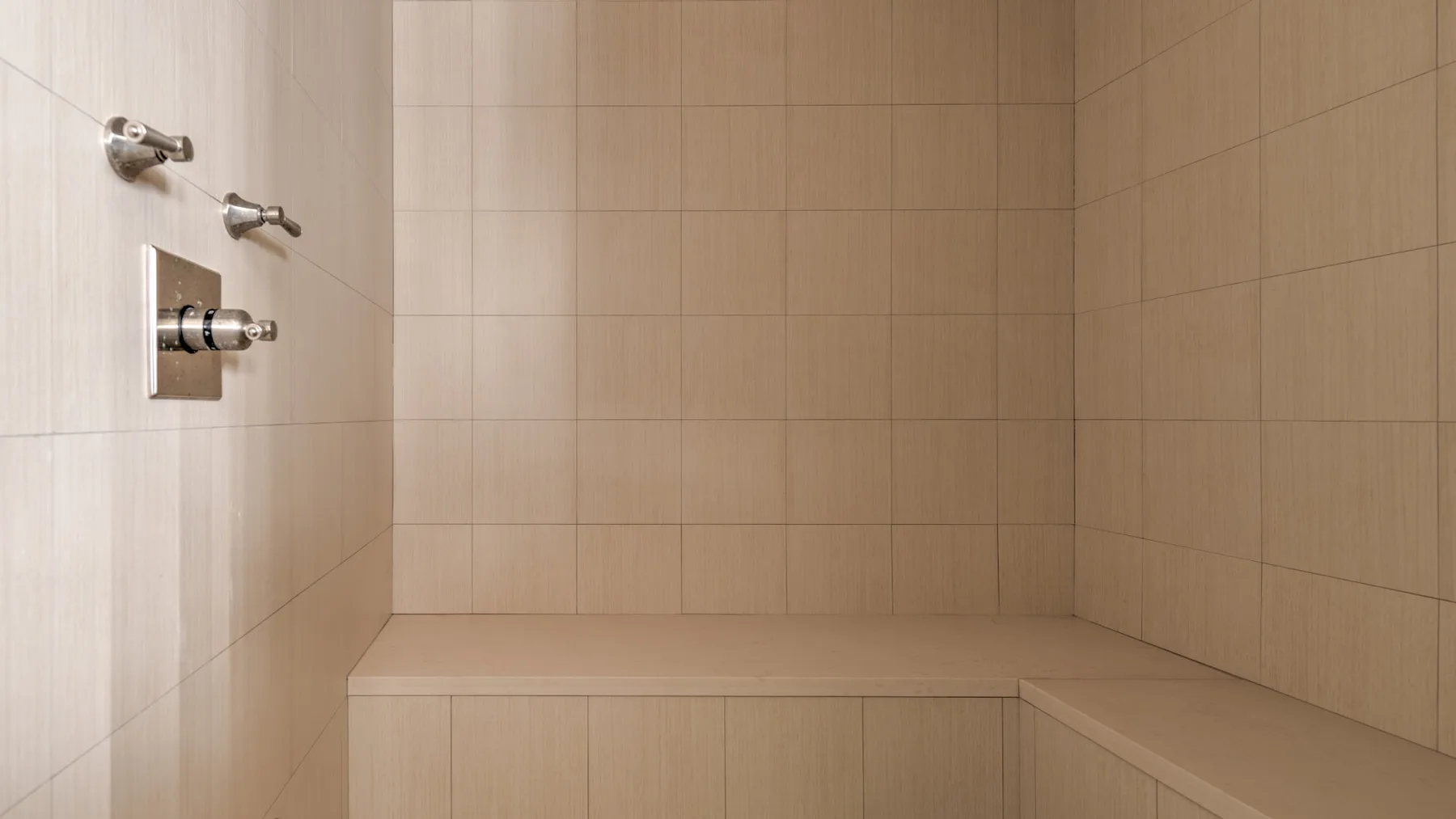 Una zona de ducha con azulejos y controles metálicos en la pared.