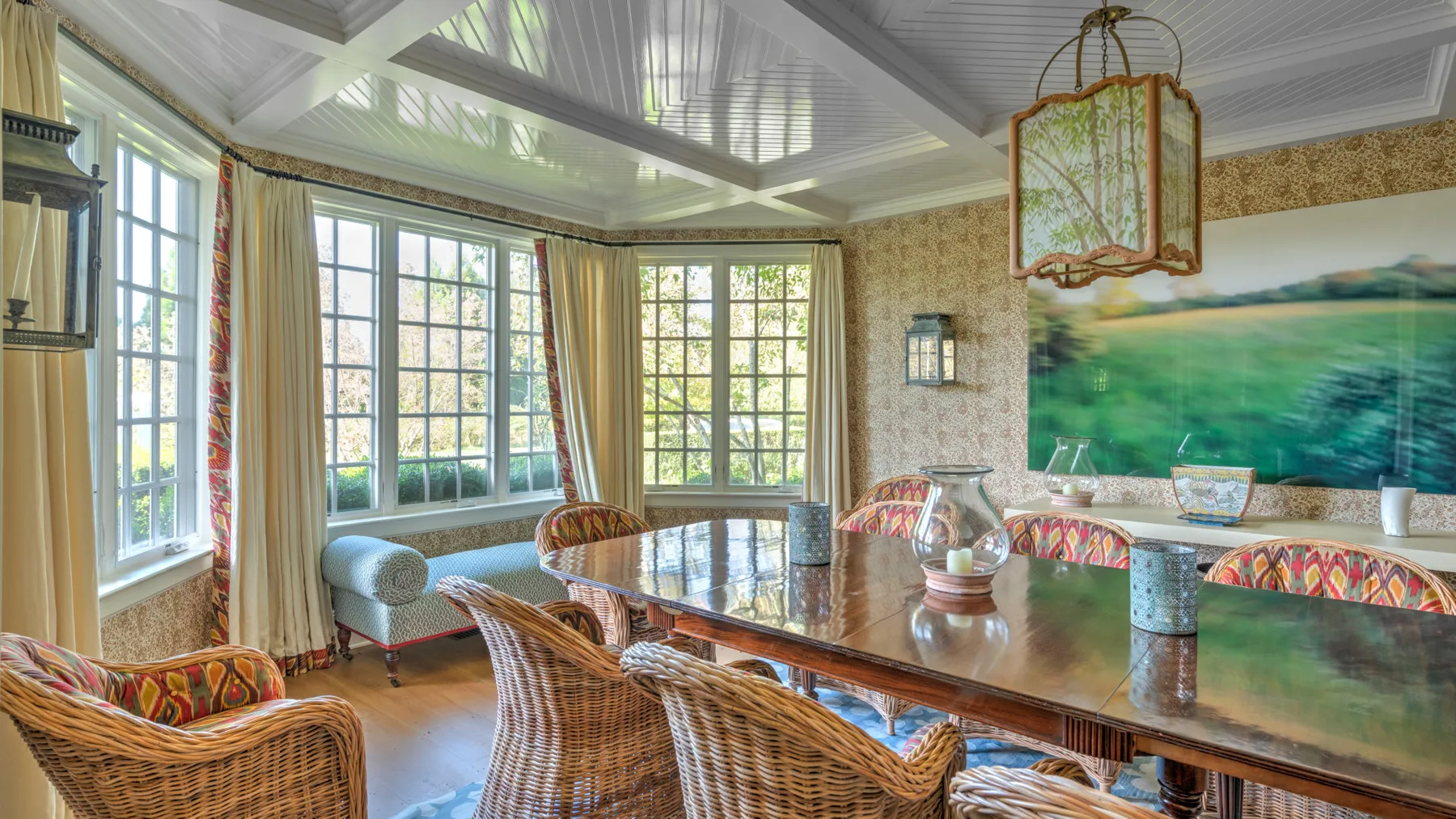 Un comedor luminoso con una mesa larga, asientos de mimbre y grandes ventanas.