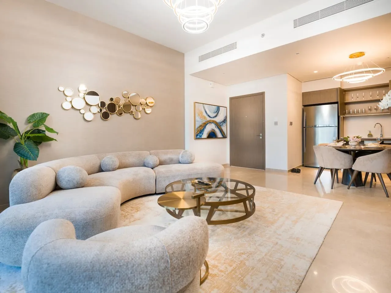 A bright living room with curved seating, a glass coffee table, and an open kitchen.