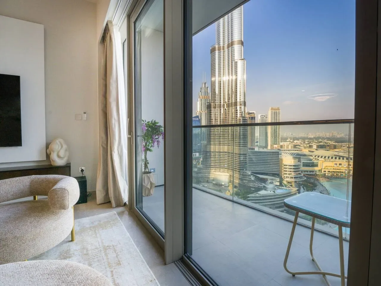 A bright living area opens onto a balcony with a city skyline view.
