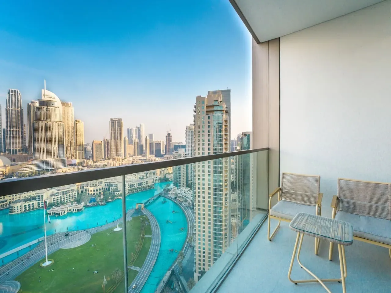 A balcony overlooks a turquoise pool, green lawn, and city skyline.