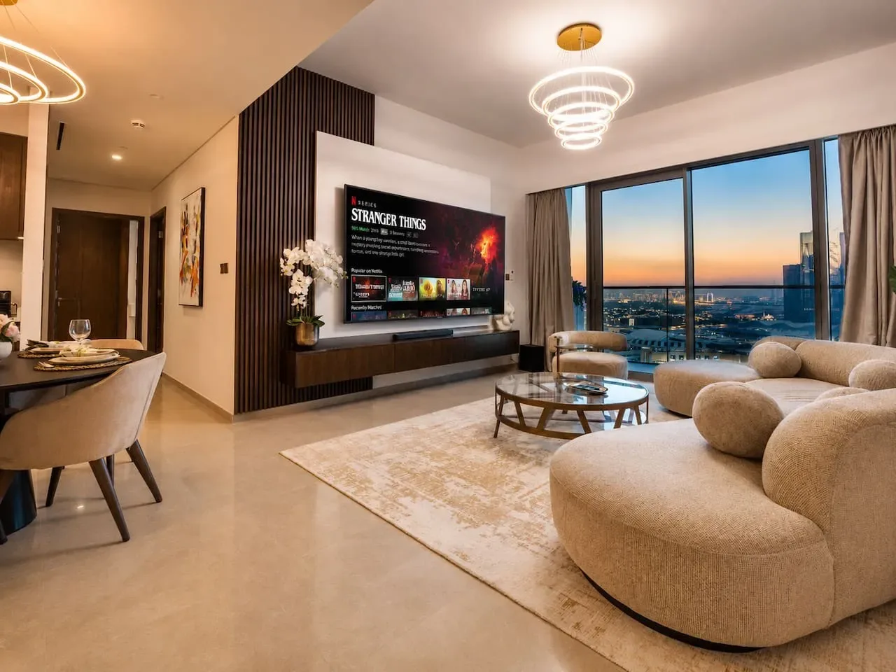 A modern living room with a television, seating, and large windows overlooking the city.