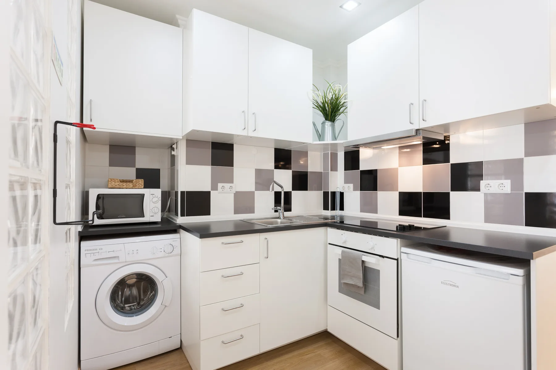 Una cocina luminosa con armarios blancos, una lavadora y un horno integrado.