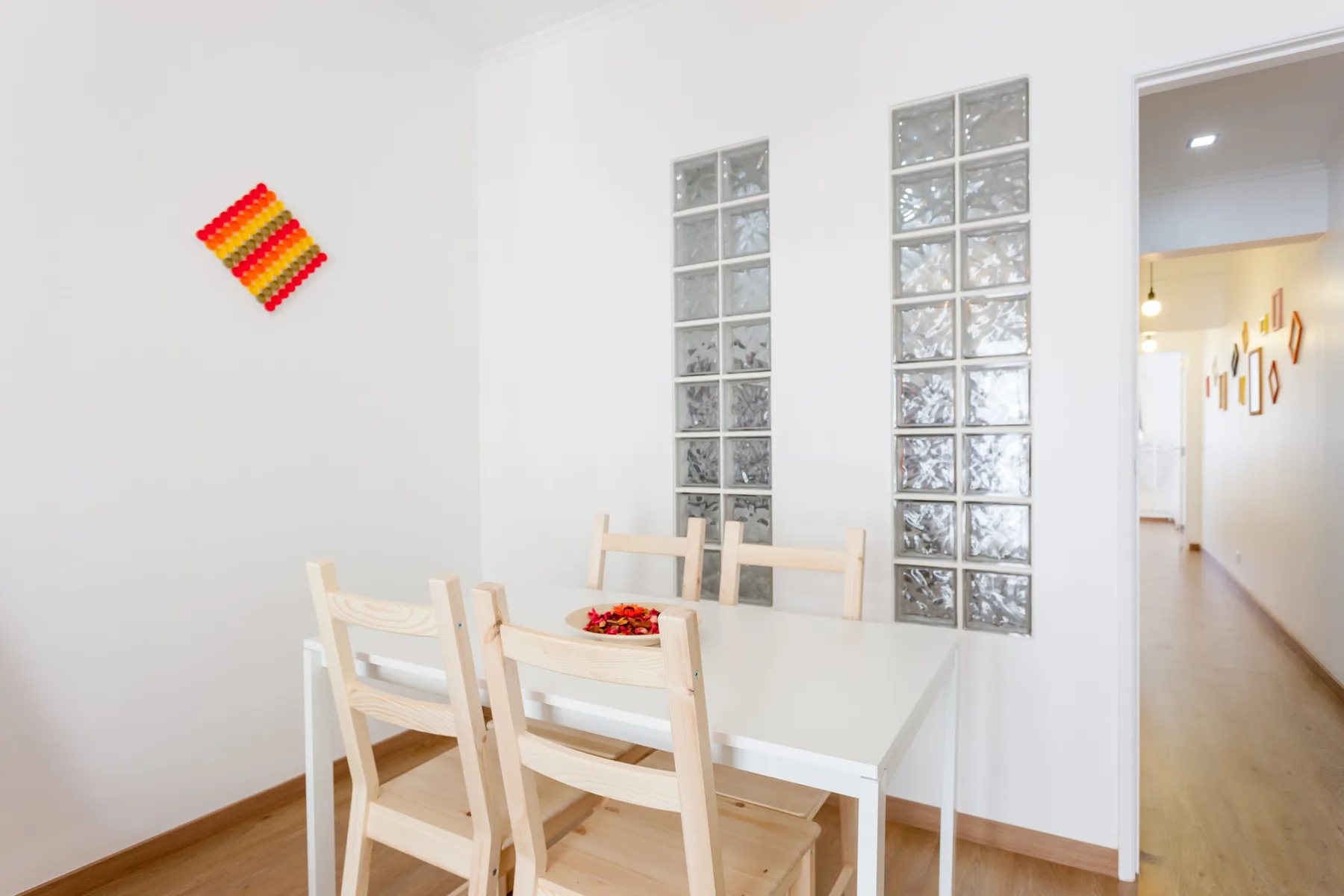 Un comedor luminoso con una mesa blanca y asientos de madera junto a ventanas de bloques de vidrio.
