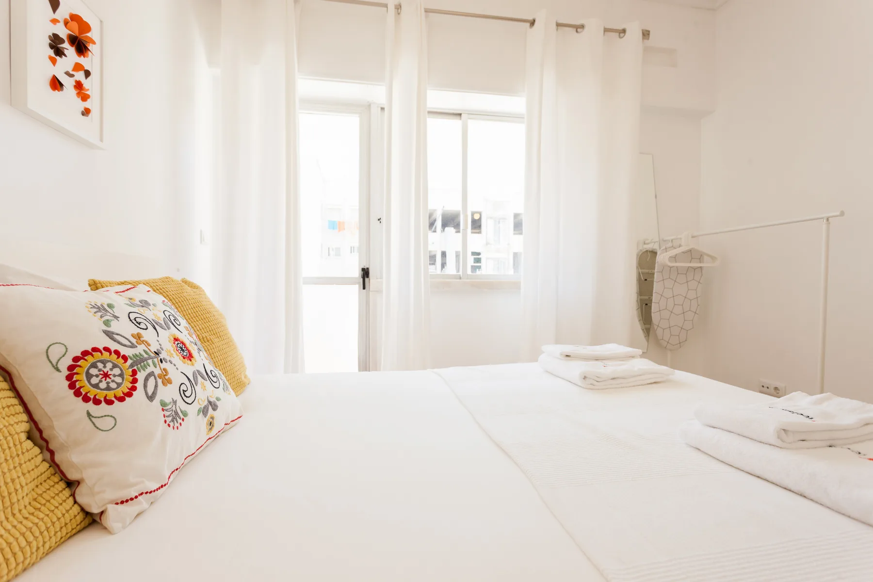 A bright bedroom with a neatly made bed beside tall windows.