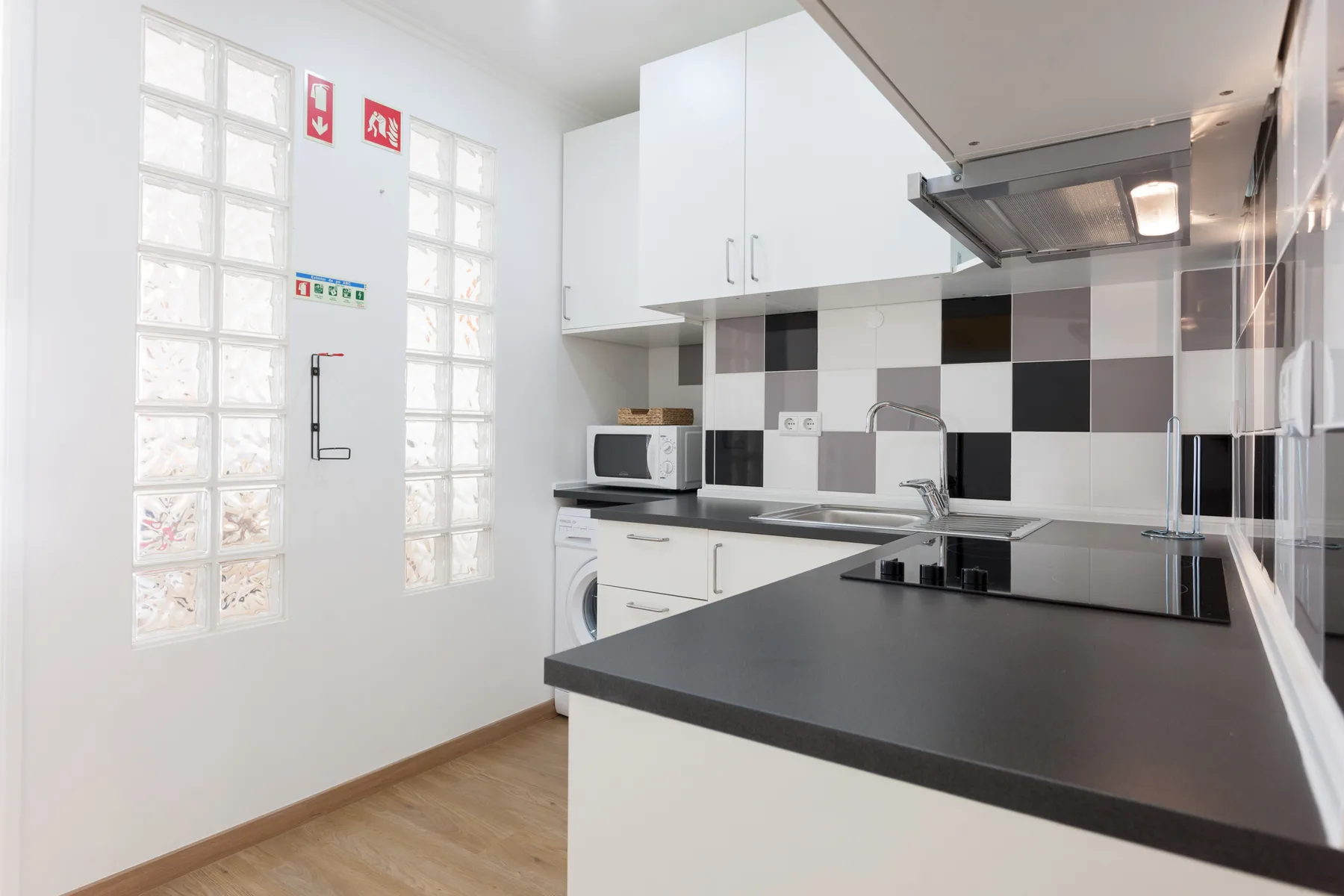 Una cocina luminosa con gabinetes blancos, encimeras oscuras y un salpicadero de azulejos.