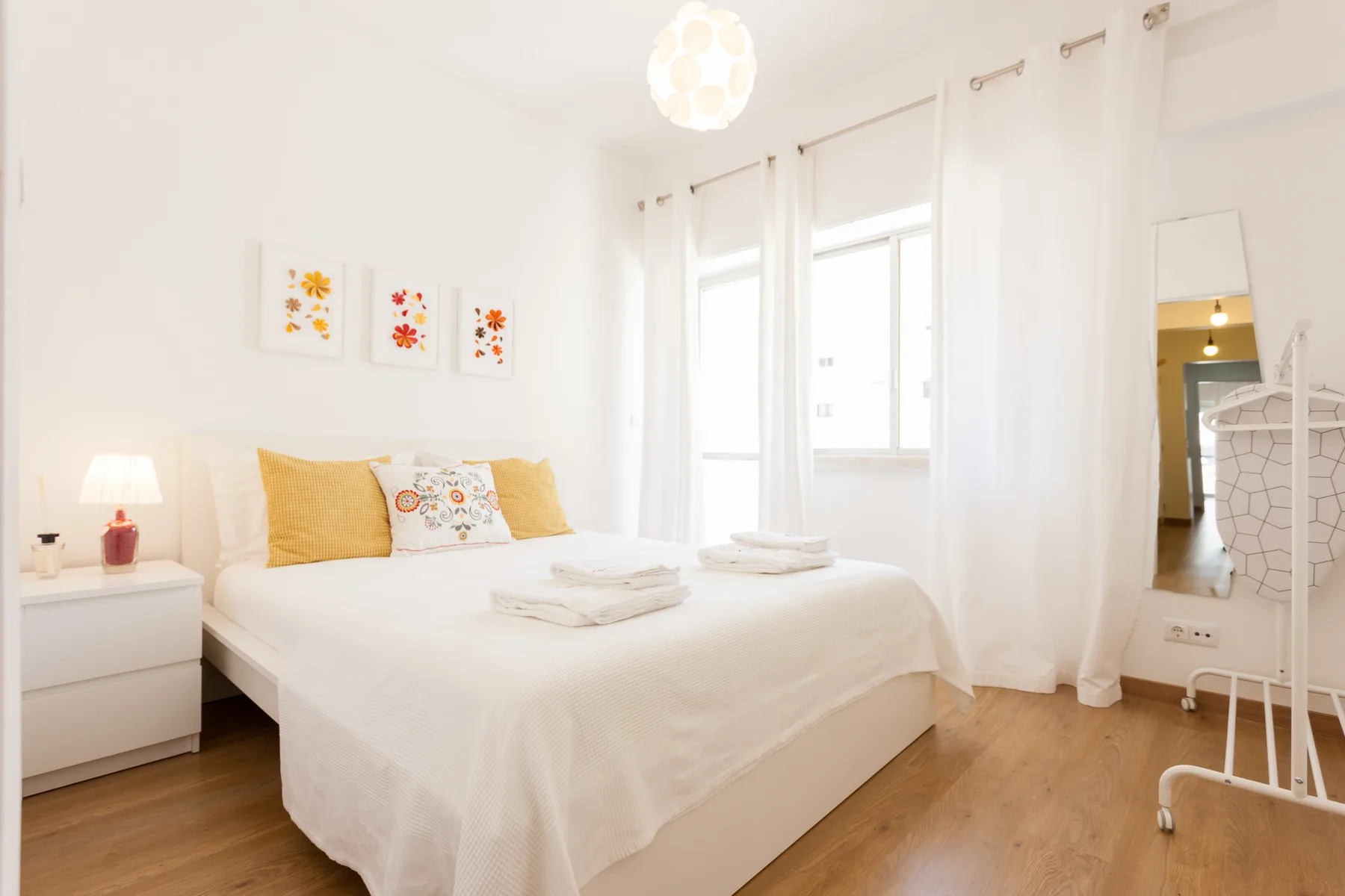 Un dormitorio luminoso con una cama bien hecha y cortinas blancas.