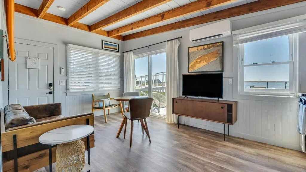 A bright living room with seating, a television, and large windows overlooking the water.