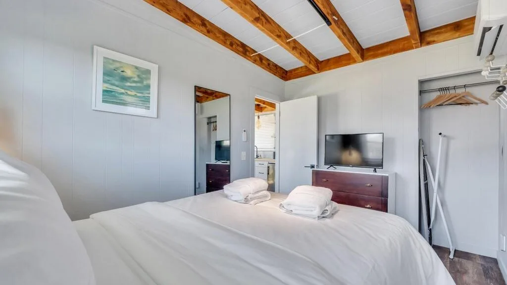 A bright bedroom with a neatly made bed and exposed wooden ceiling beams.