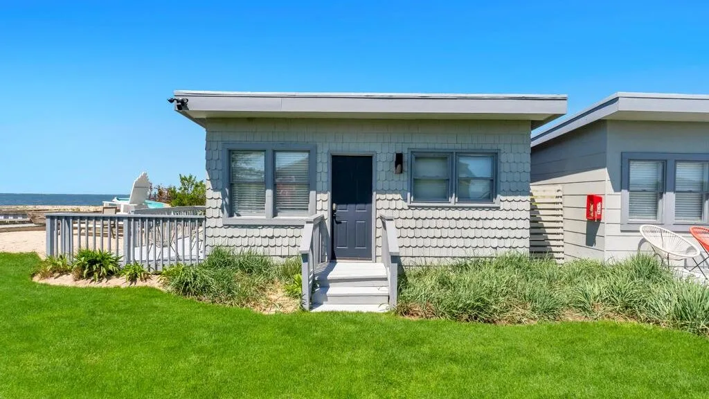 A small coastal building with a dark entrance door and windows faces a lawn.