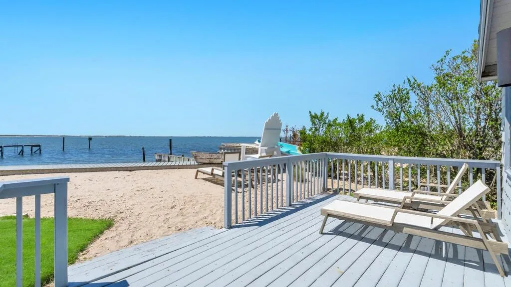A sandy waterfront deck with lounge seating overlooks the water.