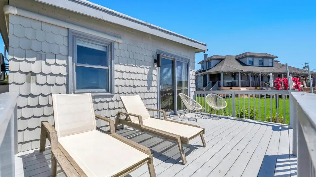 A sunny outdoor deck with lounge seating overlooks neighboring houses.