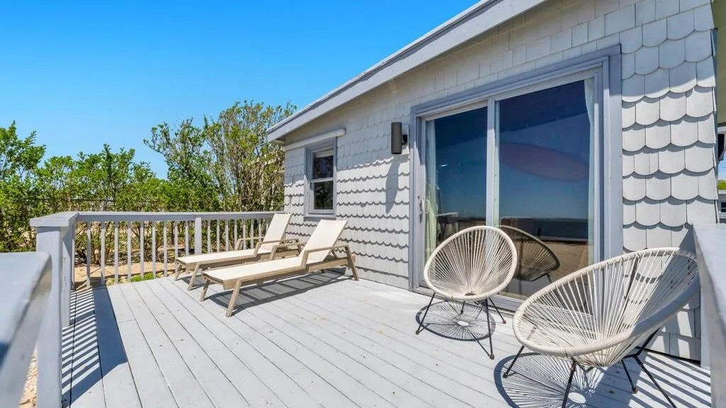 A sunny outdoor deck with lounge seating beside a house.