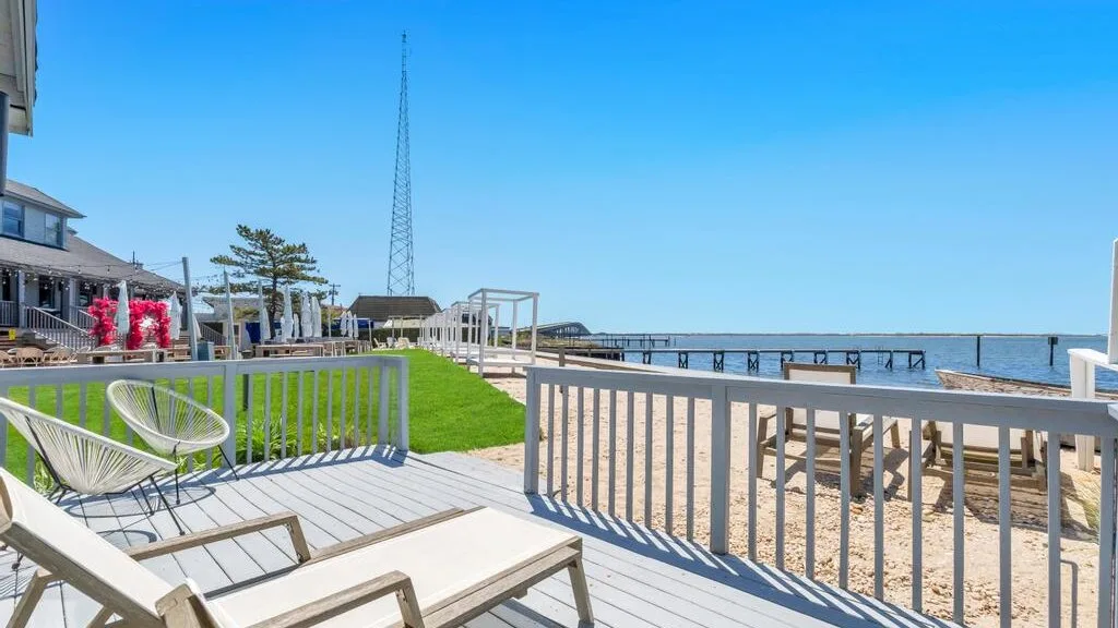 A waterfront deck overlooks a sandy shoreline and a long pier.