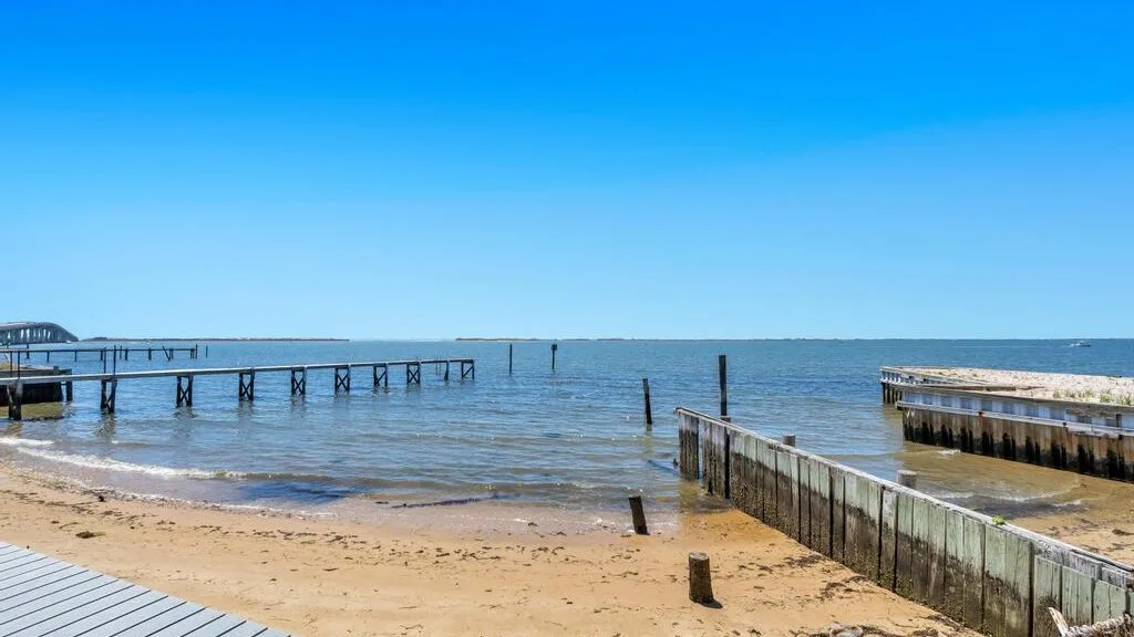 A sandy beach meets calm water beside weathered wooden piers.