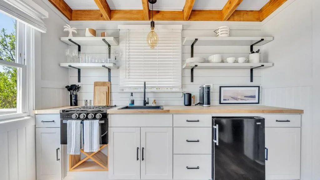 A bright kitchen with white cabinets, open shelves, and a central window.