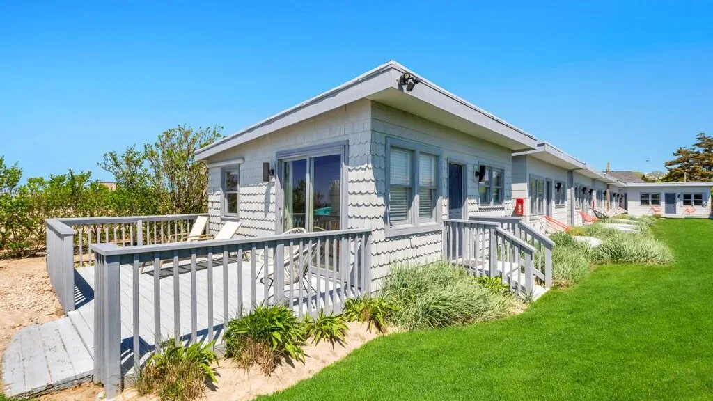 A low coastal-style building with a gray-railed deck beside a green lawn.