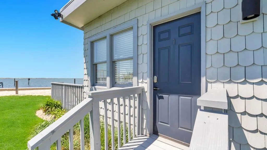 A small exterior porch with a blue door and white railing overlooks a grassy area.