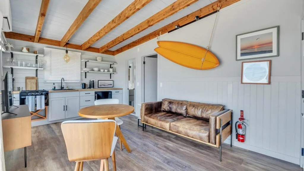 A living area with a brown sofa and a hanging orange surfboard.