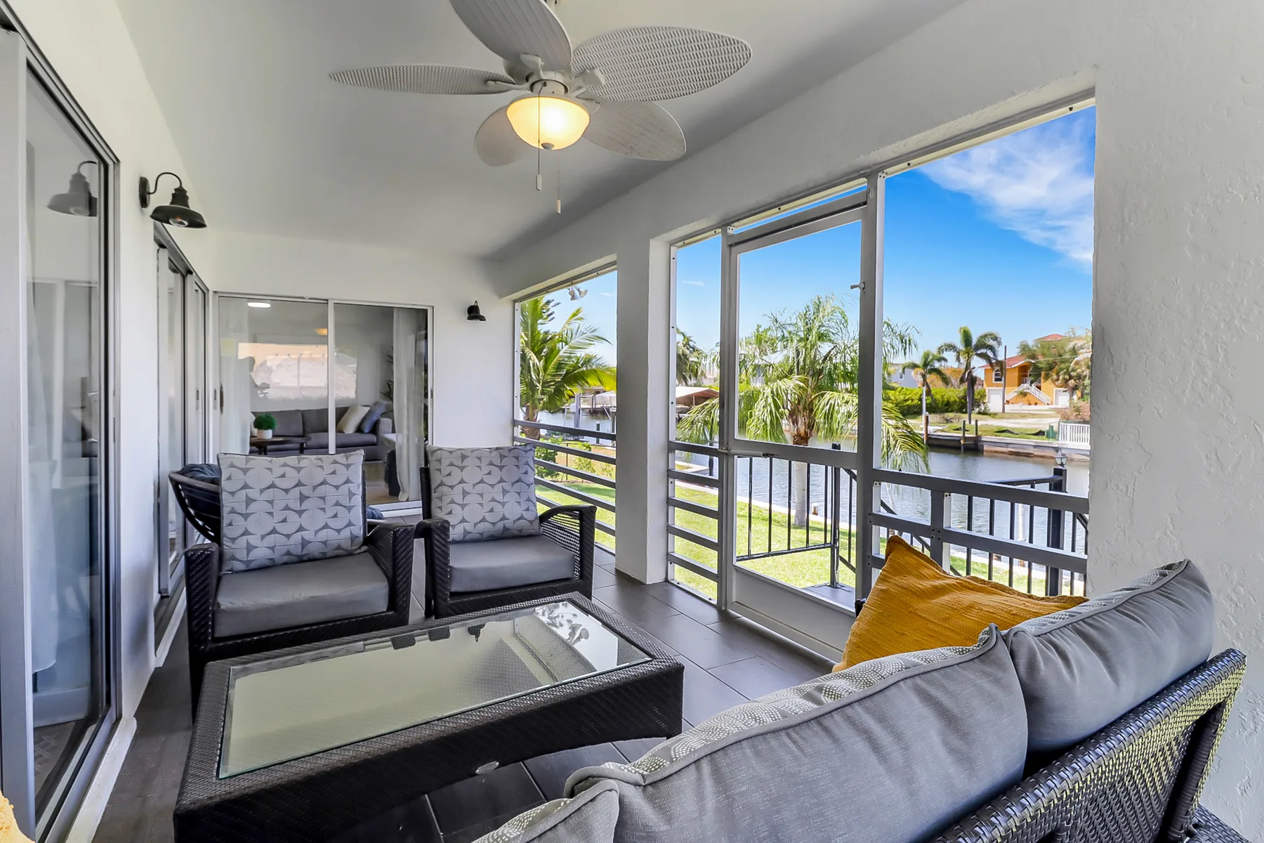 A covered seating area opens onto a balcony with views of palm trees.
