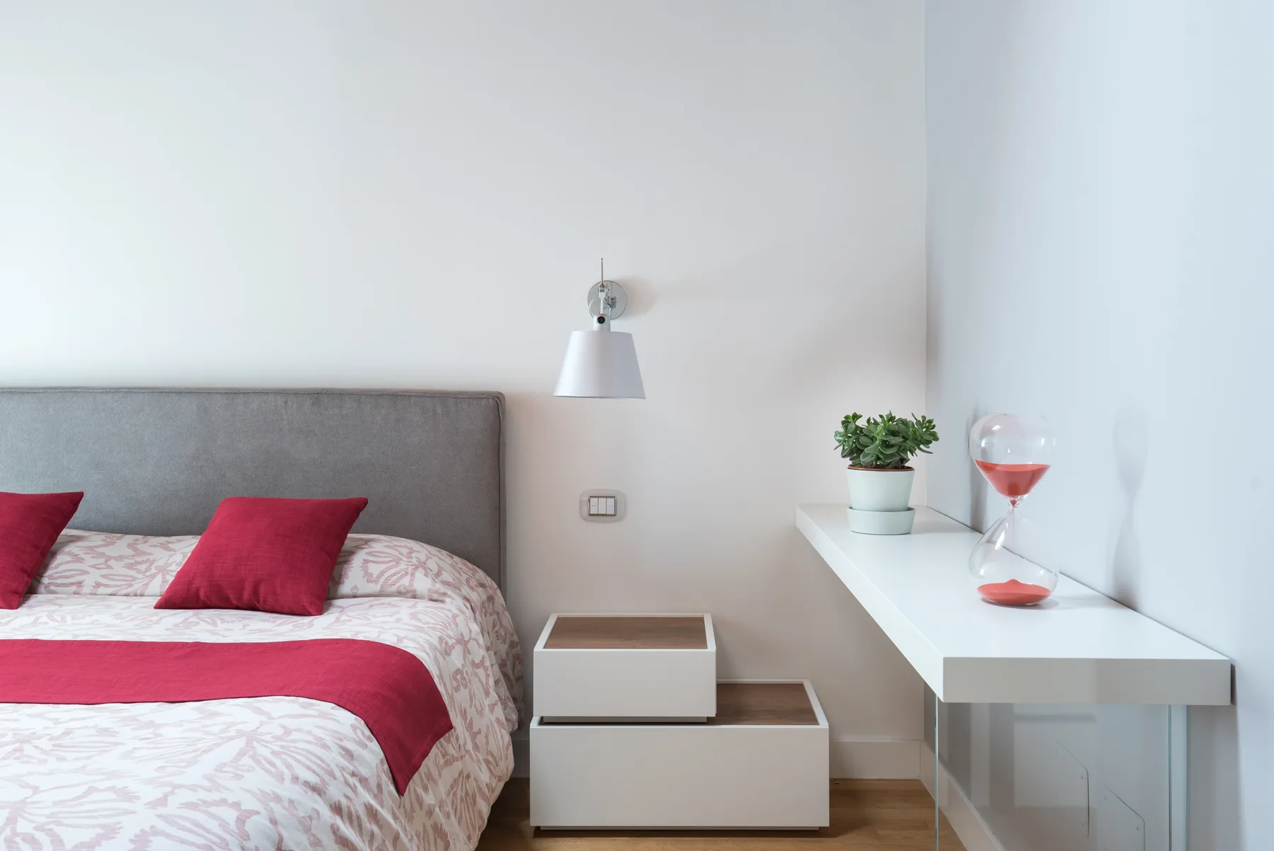 Un dormitorio con una cama, ropa de cama roja y un escritorio blanco.